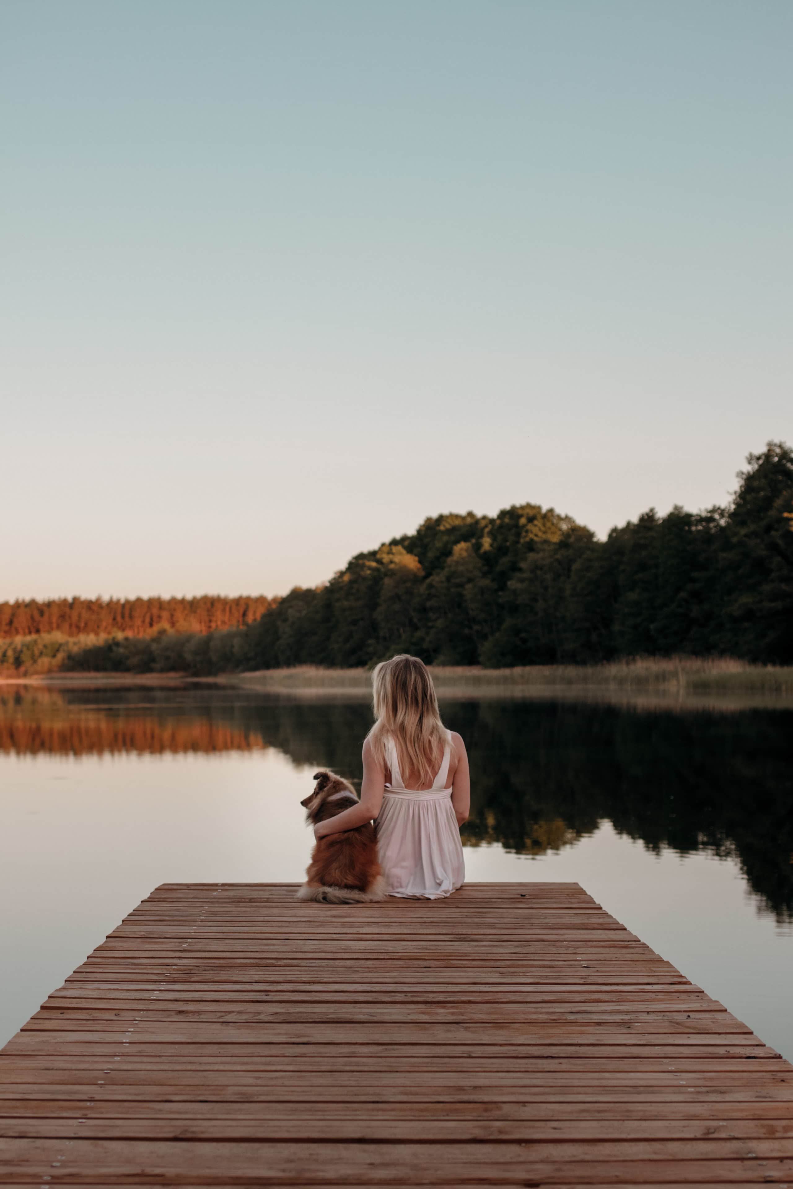 sonnenaufgang über see steg frau hund